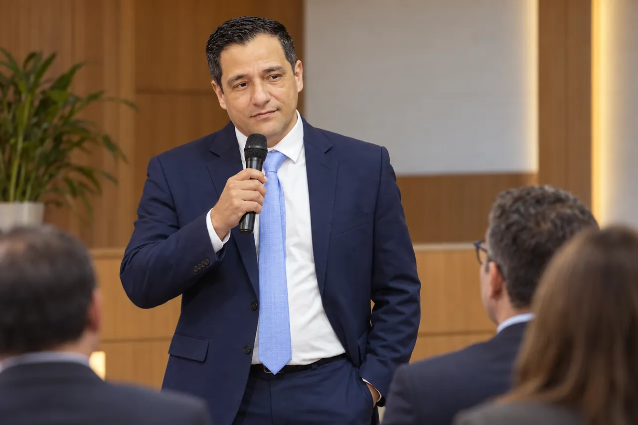 Anderson Elias, de terno azul-marinho, fala ao microfone para empresários e advogados sentados em um auditório com paredes de madeira.